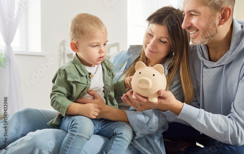 фотографія Happy young mother, father and adorable little son holding toy pink piggy bank,