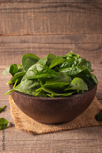 Green baby spinach leaves in wooden bowl on wooden background. Organic food concept. 