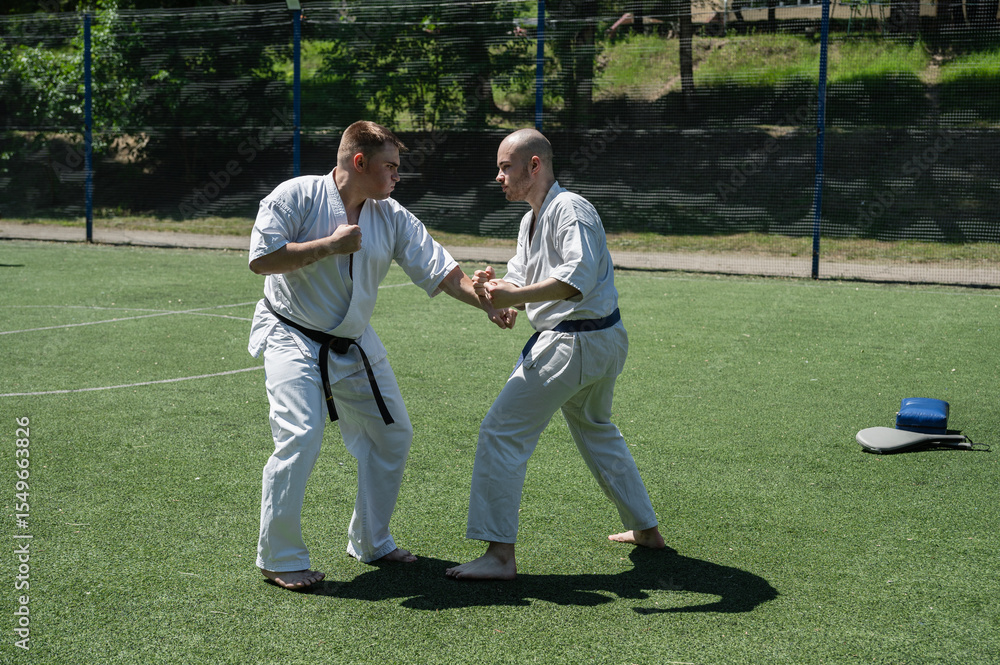 Obraz premium Karate fighters practicing blocking and striking techniques outside.