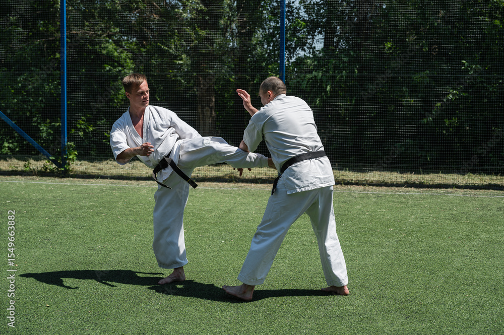 Obraz premium Man in white karate gi delivering a front kick to his sparring partner.