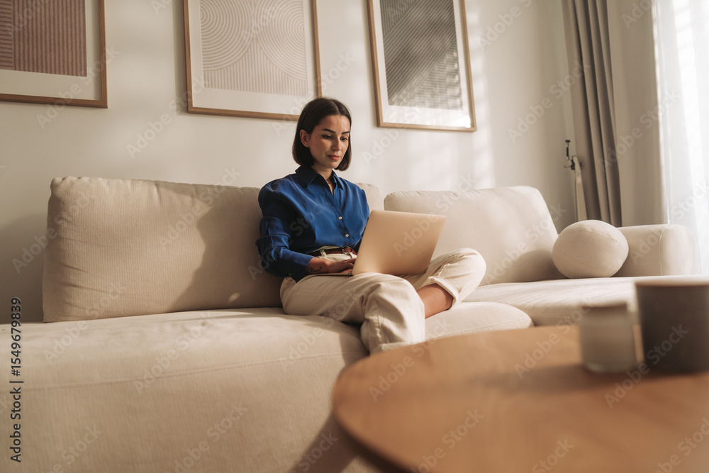 A Woman Engaged in Remote Work on Her Laptop While Relaxing in a Cozy Living Room A Woman Engaged in Remote Work on Her Laptop While Relaxing in a Cozy Living Room