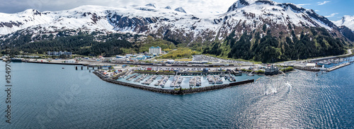 wide angle panoramic aerial landscape view of Whittier Cityscape with Harbor and Port located at head of Passage Canal in Alaska, USA, with snow covered mountain landscape in background 