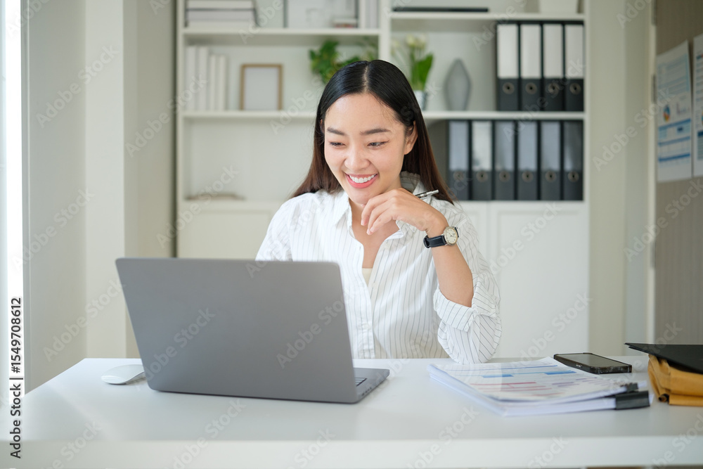 Smiling Asian businesswoman working on a laptop at a modern office desk. Smiling Asian businesswoman working on a laptop at a modern office desk.