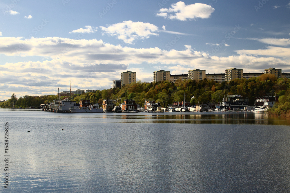 Fototapeta premium Residential buildings of Stockholm across water with tree-lined shoreline under a partly cloudy spring sky