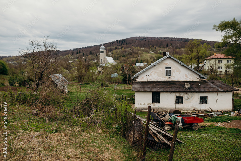 Fototapeta premium Spring landscape with a Christian church nestled among hills and forest. Tree branches frame the frame, creating a cozy, spiritual atmosphere