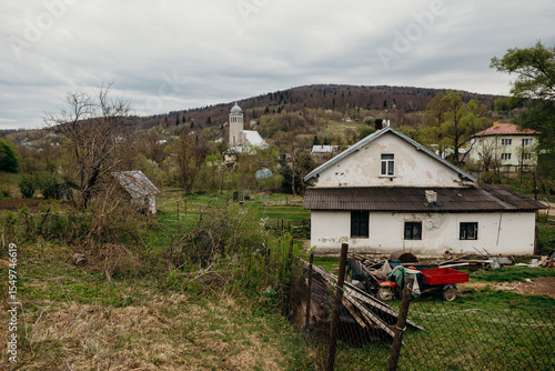 Spring landscape with a Christian church nestled among hills and forest. Tree branches frame the frame, creating a cozy, spiritual atmosphere