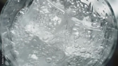 Pouring sparkling water over ice cubes in an elegant glass, close-up.