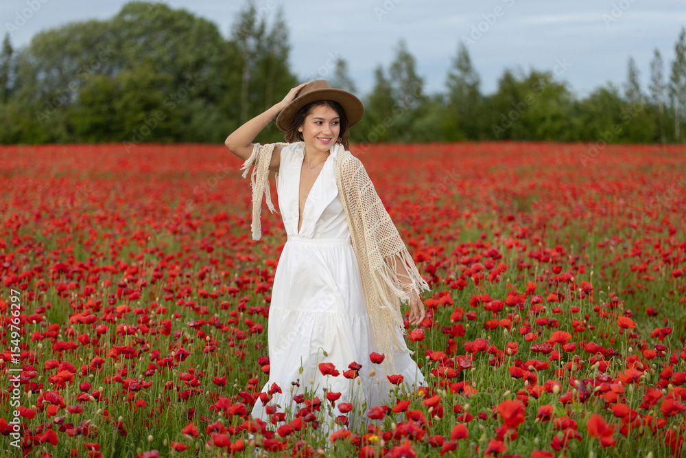 Young woman in a white dress and hat posing among summer poppies Young woman in a white dress and hat posing among summer poppies