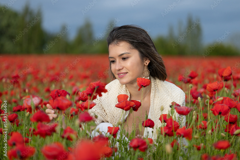 Naklejka premium Young woman in a white dress posing among summer poppies