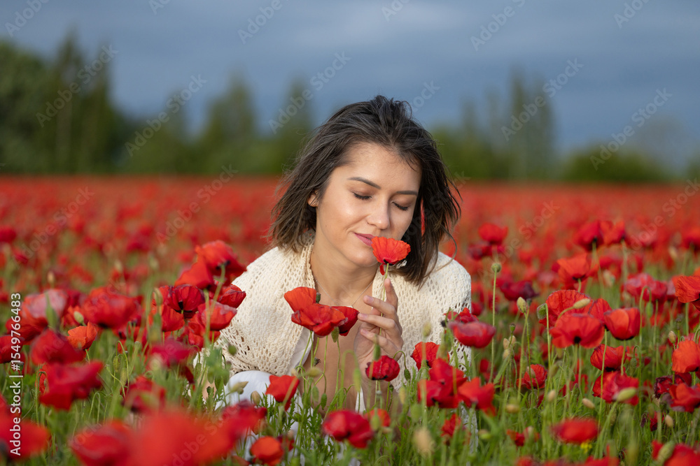 Naklejka premium Young woman in a white dress smells the poppies in a summer field