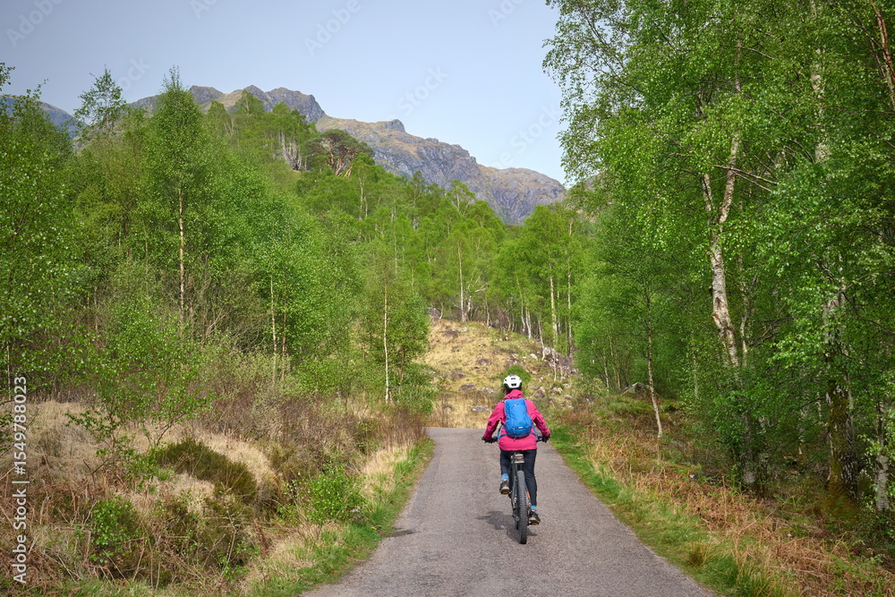 active senior woman riding her electric mountain bike in the Glen Nevis valley below Ben Nevis summit in the highlands near Fort William in Scotland, UK active senior woman riding her electric mountain bike in the Glen Nevis valley below Ben Nevis summit in the highlands near Fort William in Scotland, UK
