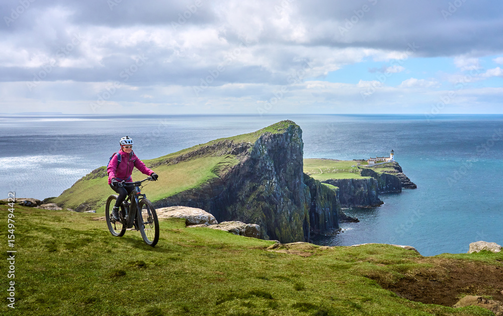 Fototapeta premium active senior woman riding her electric mountain bike on the cliffs of nest point lighthouse on the Isle of Skye in Scotland, UK