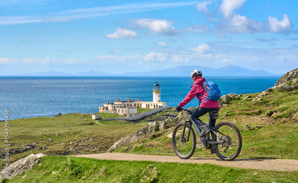 Fototapeta premium active senior woman riding her electric mountain bike on the cliffs of nest point lighthouse on the Isle of Skye in Scotland, UK