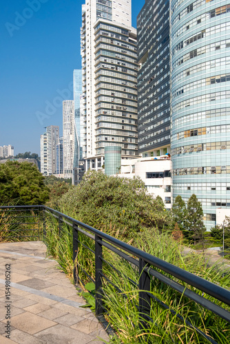Contemporary skyline of Santa Fe seen from La Mexicana Park with lush greenery, reflective glass towers and clear blue sky in Mexico City, ideal for themes of urban development