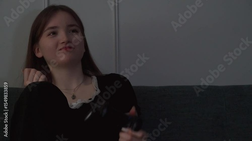 Young teen girl playing video games sitting cross-legged on couch showing intense emotional reactions while immersing herself in digital gameplay with concentrated concentration