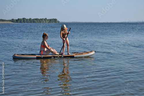 A girl and a woman are riding a SUP board.