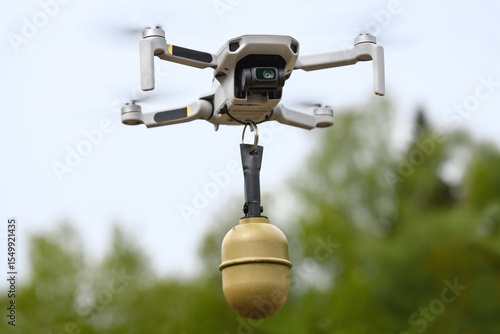 Small Flying unmanned aerial vehicle in flight mode with camera with a grenade attached outdoor on green forest background