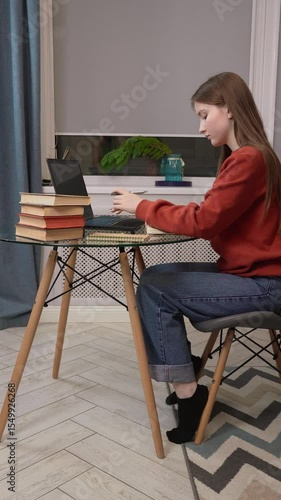 Young teenage girl sitting at desk, using laptop and taking notes, emphasizing the importance of ergonomics. Prepares for exams or homeschooling. vertical video