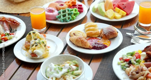 Luxurious hotel breakfast buffet with fresh pastries, eggs Benedict, colorful waffles, fruit, juice on wooden table. Indulgent dining, vibrant culinary experience, perfect for travelers.