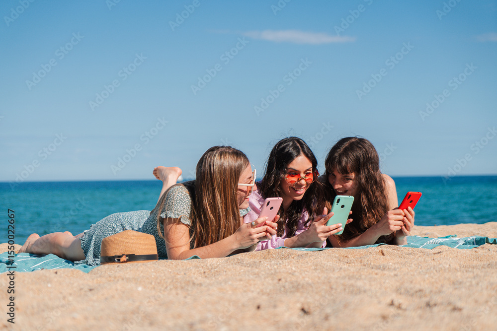 A delightful moment shared by three young women as they explore their smartphones while lying on the warm sand at the beach. Enjoying their time together, they are captivated by their mobile devices. A delightful moment shared by three young women as they explore their smartphones while lying on the warm sand at the beach. Enjoying their time together, they are captivated by their mobile devices.