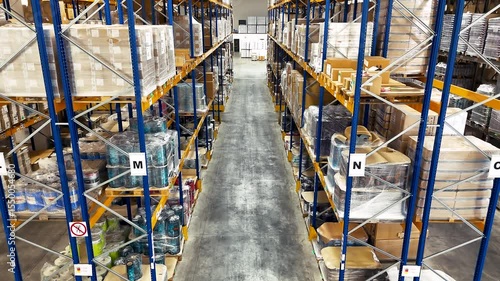 Rise up and aerial drone video of large indoor storage area with packed goods on blue shelves. Storage of manufactured goods on the warehouse premises. Top view
