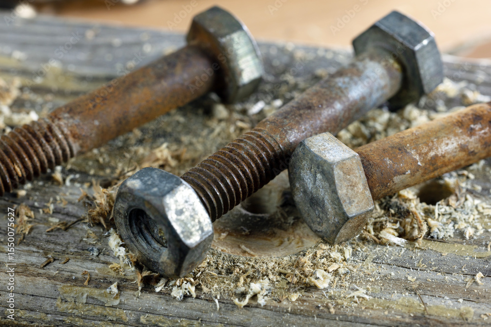 Close-up of rusty bolts and nuts on a wooden surface. Shavings and drill marks are visible, indicating recent use in a woodworking project. Close-up of rusty bolts and nuts on a wooden surface. Shavings and drill marks are visible, indicating recent use in a woodworking project.