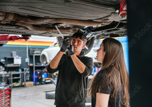Foto Young mechanic woman watches attentively as a colleague works under a lifted veh