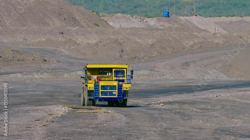 An operator is driving the huge dump truck at the open pit mine. Dump truck used for material transportation at the mine. Yellow dump truck is passing through the gold mine. Quarry. Gold excavation
