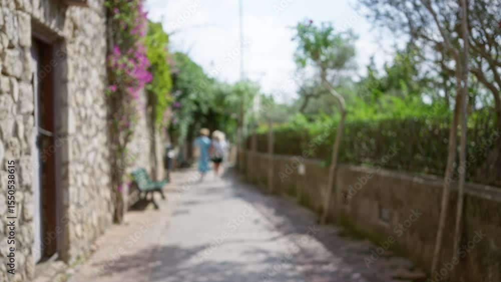 Woman strolling along a picturesque capri street, surrounded by lush greenery and stone walls, creating a serene and luxurious italian island vibe with defocused background. Woman strolling along a picturesque capri street, surrounded by lush greenery and stone walls, creating a serene and luxurious italian island vibe with defocused background.