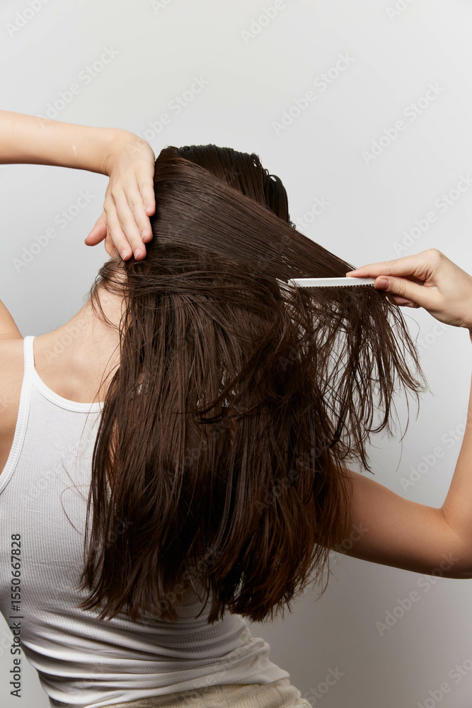 Fototapeta premium Hair care, grooming, young woman combing hair, healthy long hair, minimalist background, white backdrop, casual style, beauty routine, attention to hair texture, personal care, satisfaction
