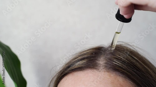 Young caucasian female applying hair serum with dropper for scalp nourishment and hair care routine.