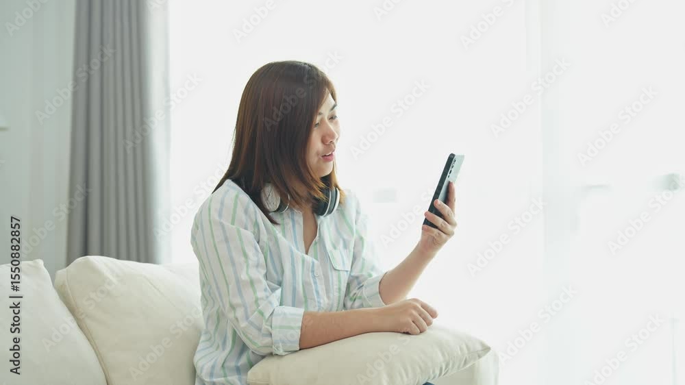 Young woman enjoying a video call at home while sitting on a cozy sofa, showcasing happiness and connection through smartphone technology Young woman enjoying a video call at home while sitting on a cozy sofa, showcasing happiness and connection through smartphone technology