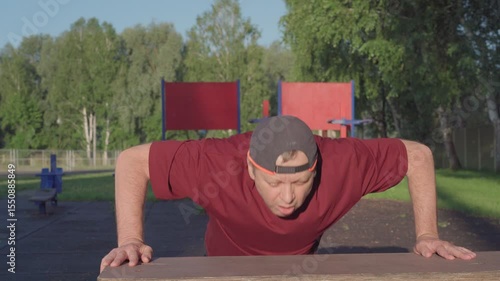 An elderly man is training on a sports ground. Strength exercise - push-ups.