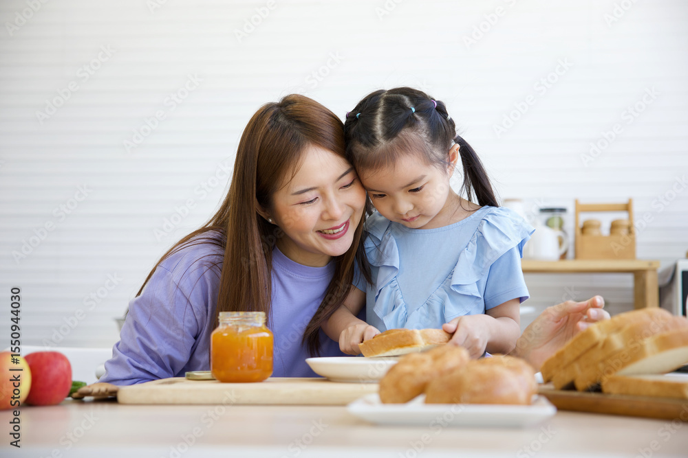 kid putting orange jam on bread toast with her mother in the kitchen kid putting orange jam on bread toast with her mother in the kitchen