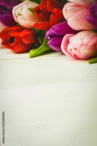 Fototapeta Naklejka Na Ścianę i Meble -  Cluster of multicolored tulip flowers is being shown in flat vector style on light wooden tabletop