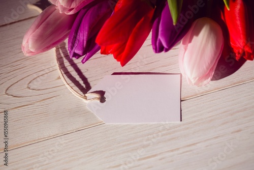 Fototapeta Naklejka Na Ścianę i Meble -  Tulip cluster is casting soft shadows on wooden tabletop in flat design, with blank gift tag