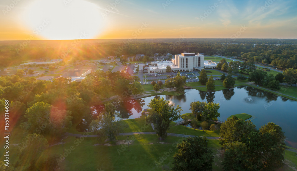 Fototapeta premium Aerial view of a hospital complex Fairview Park, Dublin, Georgia, USA. The building is surrounded by trees, a pond, and parking lots. The sun is setting in the distance.