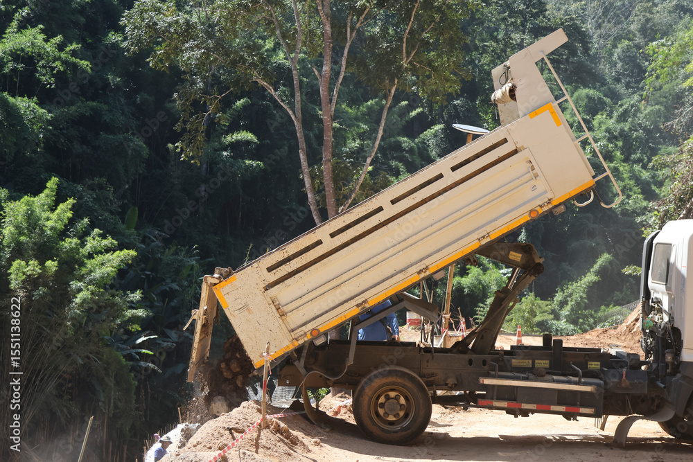 Obraz premium A white truck is dumping sand on the ground on a rural road through a forest being repaired, in the construction area of ​​a road repair contractor.