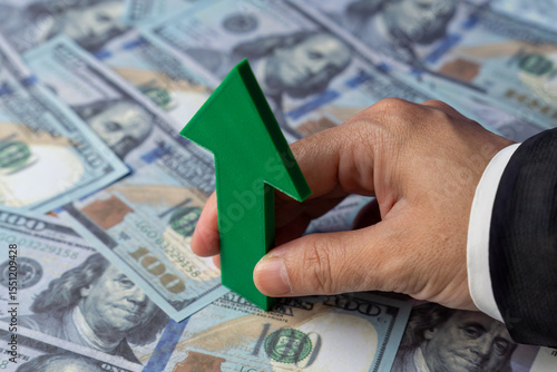 Tableau sur toile A hand holds a green upward-pointing arrow over a spread of US one-hundred dollar bills