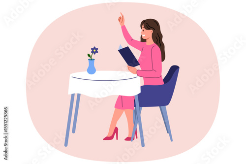 Woman restaurant visitor raises hand to call waiter and place order, sits at table and holds menu. Girl guest at elite restaurant enjoys cozy atmosphere and opportunity to eat gourmet cuisine.