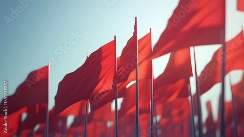 Photograph of numerous red flags billowing against a pale blue sky, creating a sense of depth and scale.