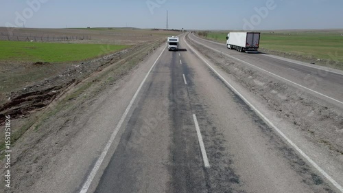 A big white motorhome is driving along the highway filming from a drone