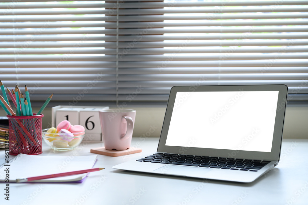 Fototapeta premium Chic feminine workspace with laptop, pastel decor, and soft lighting through window blinds