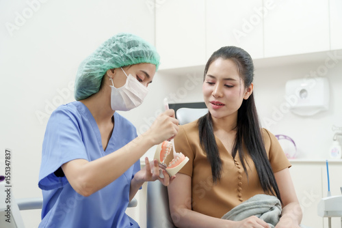 фотографія asian female dental assistant in scrub mask demonstrating proper tooth brushing