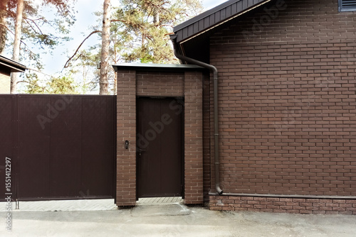 Entrance door and fence of a private brick house in the forest. Summer daytime.