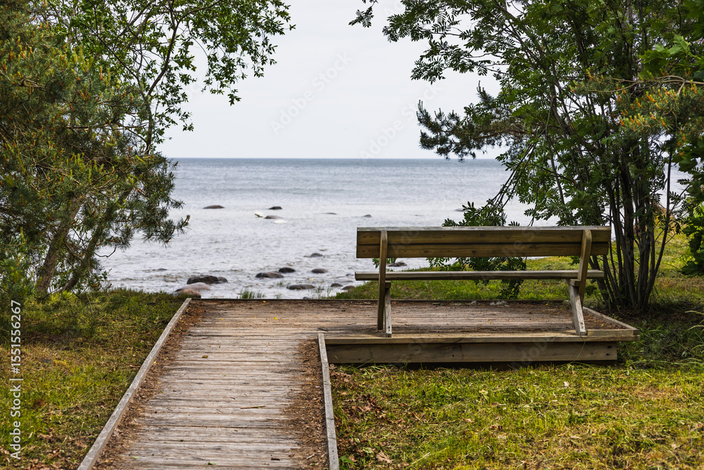 Wooden bench facing Baltic Sea at end of forest boardwalk path in Kaltene rocky coast, Latvia Wooden bench facing Baltic Sea at end of forest boardwalk path in Kaltene rocky coast, Latvia