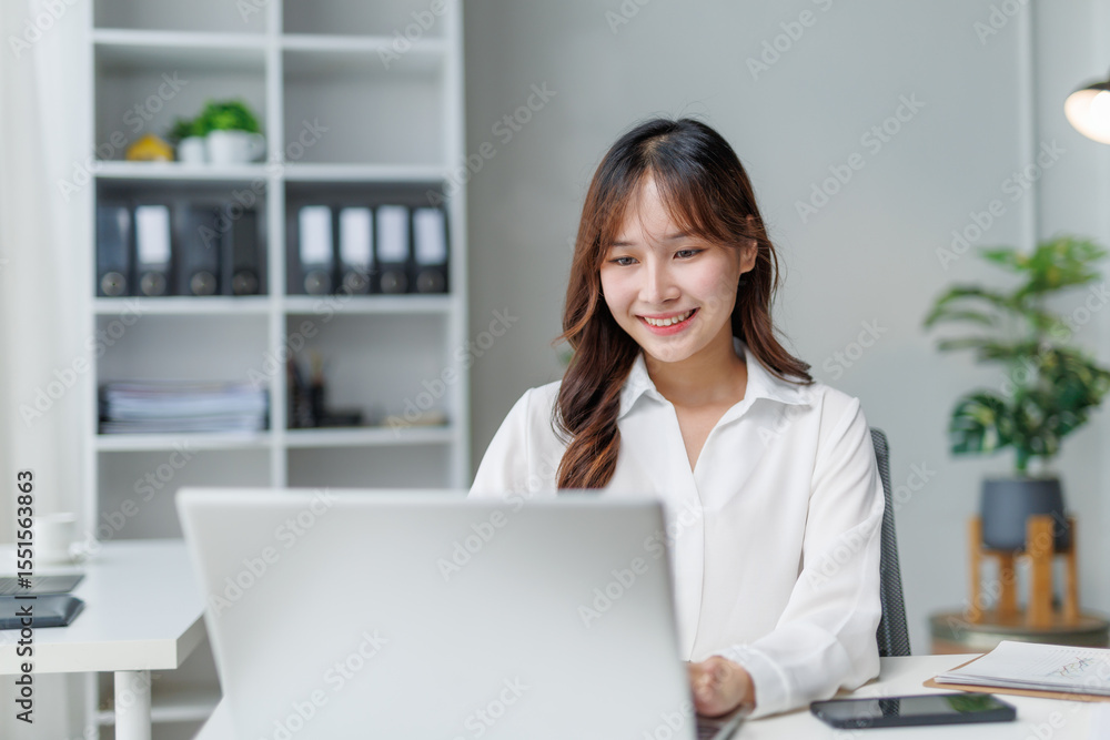 Happy manager working at a modern office desk, smiling while using a laptop and engaging with the screen in a professional setting Happy manager working at a modern office desk, smiling while using a laptop and engaging with the screen in a professional setting