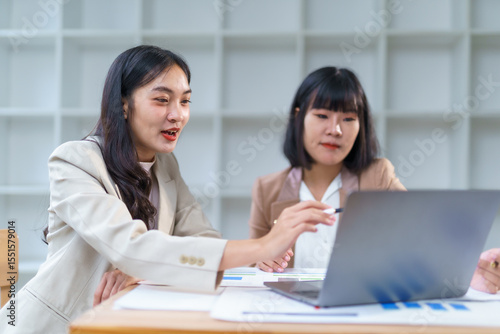 Businesswomen working together, analyzing financial data on laptop computer, discussing charts and graphs, making strategic business decisions
