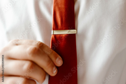 Elegant man putting tie bar on red tie