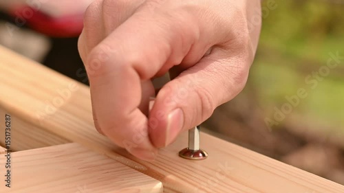 hand close-up screws a bolt with a hex key into a wooden piece of furniture, self-assembly of furniture at home